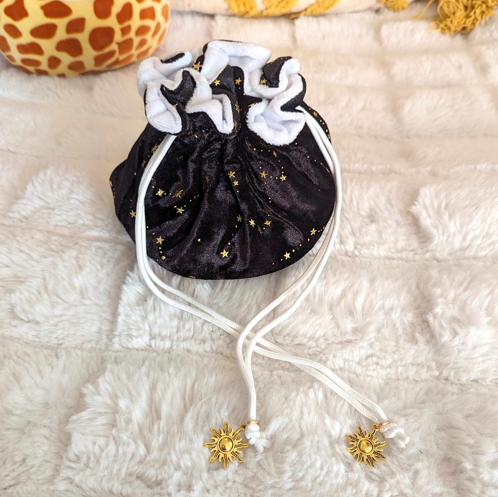 Starry black dice bag with gold stars, white plush lining, and sun charm drawstrings on plush fabric surface.