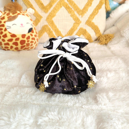 Luxurious black velvet multi-pocket dice bag with golden stars and white drawstring, adorned with sun charms, on plush background.