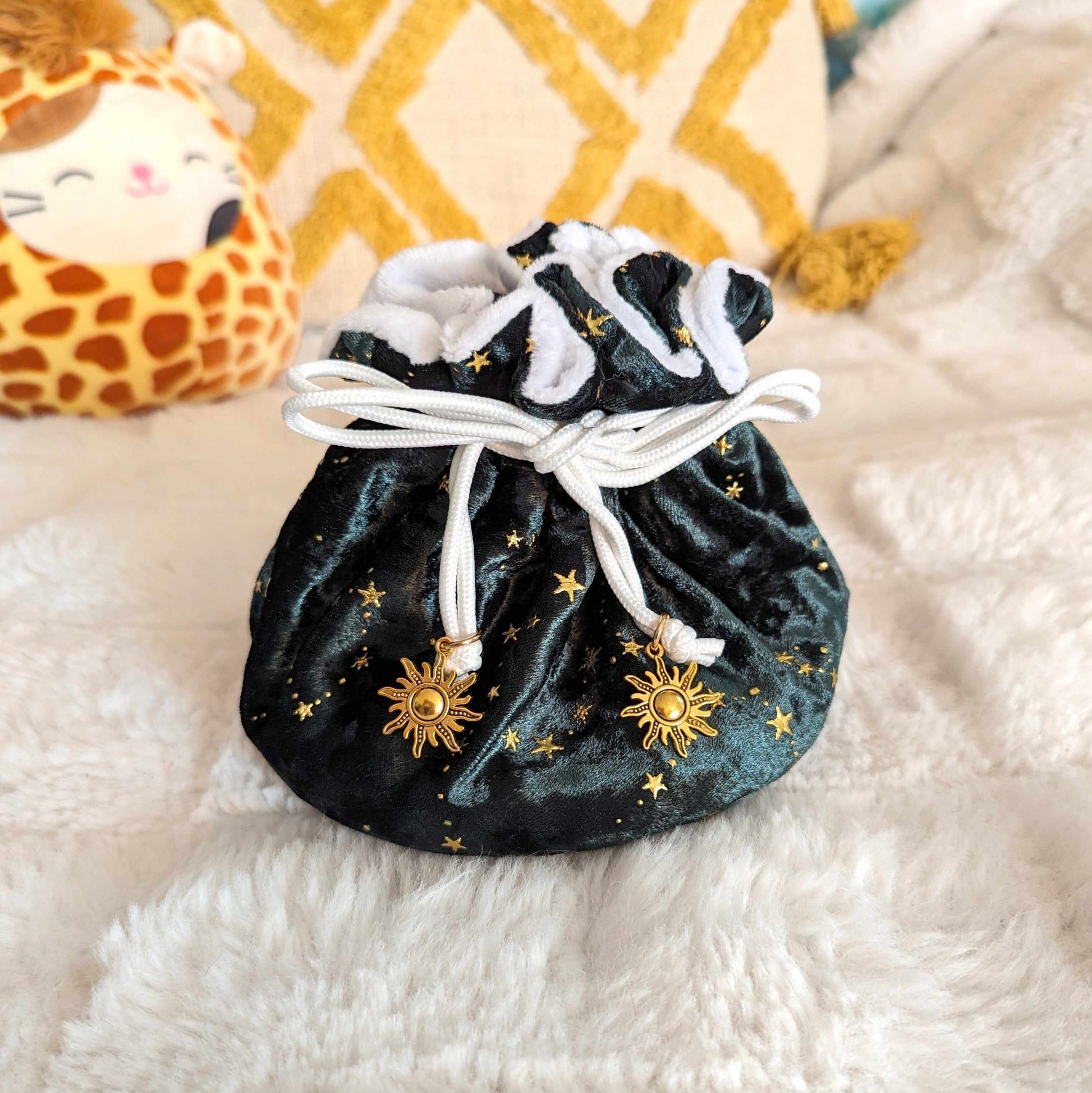 Luxurious green dice bag with gold stars, soft white lining, and sun charm drawstrings on a cozy background.