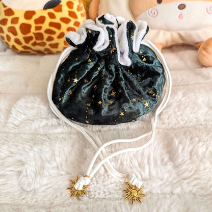 Starry green dice bag with golden stars and sun charms on white drawstrings, set on a plush background.