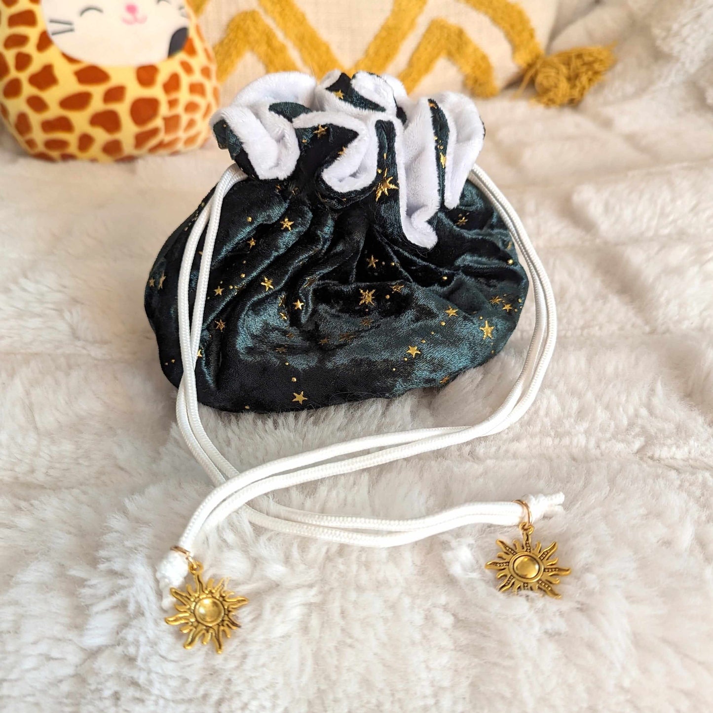 Starry green velvet dice bag with white drawstrings and golden sun charms on a plush surface.