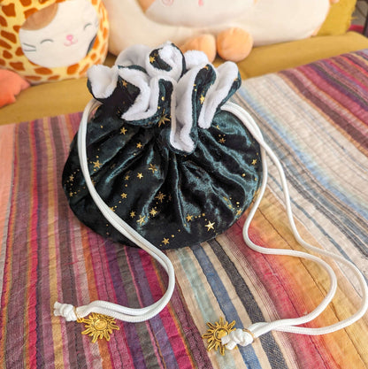 Luxurious starry green dice bag with multi pockets, golden stars, white plush lining, and sun charm drawstrings on a striped background.