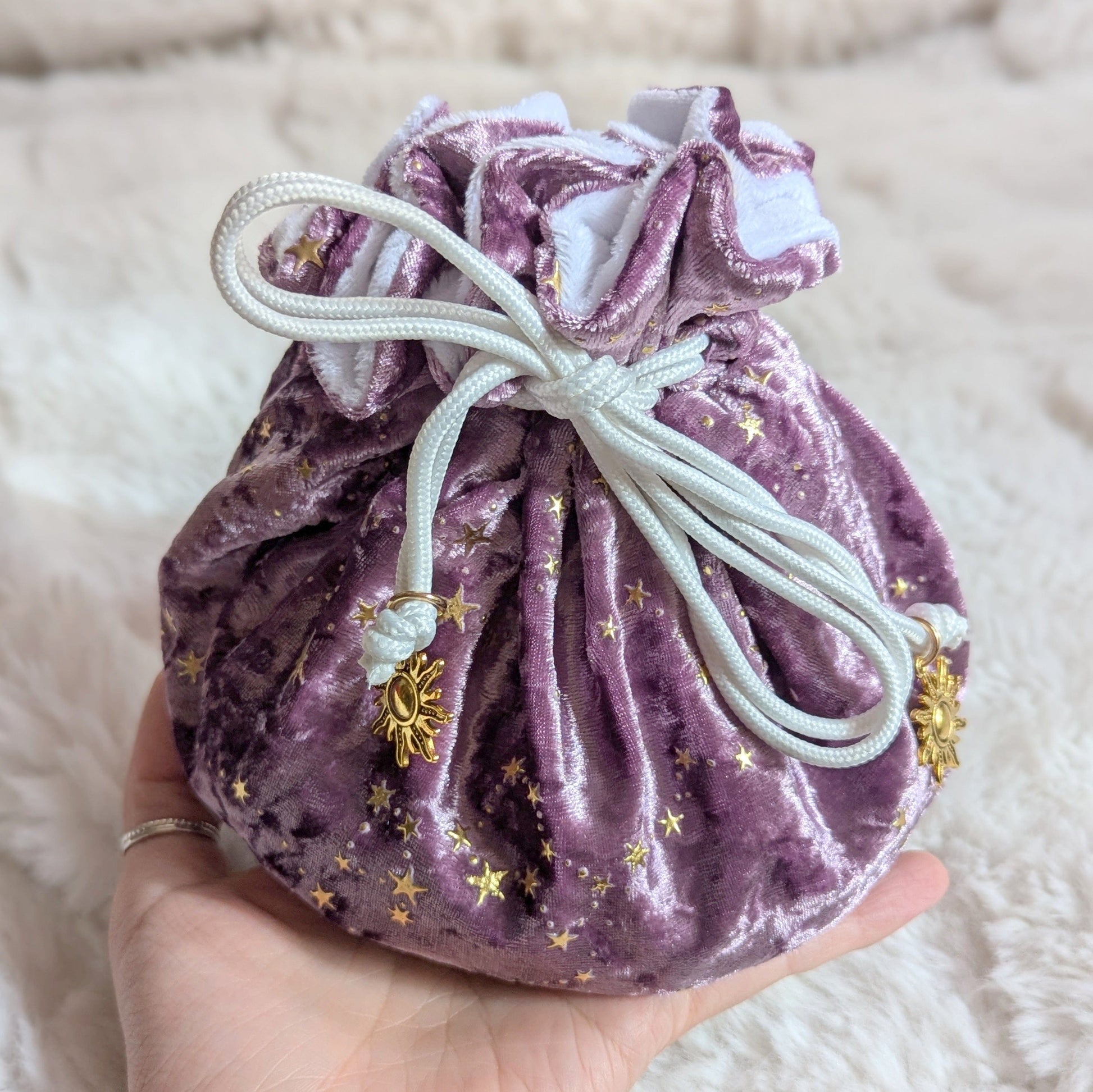 Mauve purple dice bag with gold star pattern and solar charm drawstrings held in hand