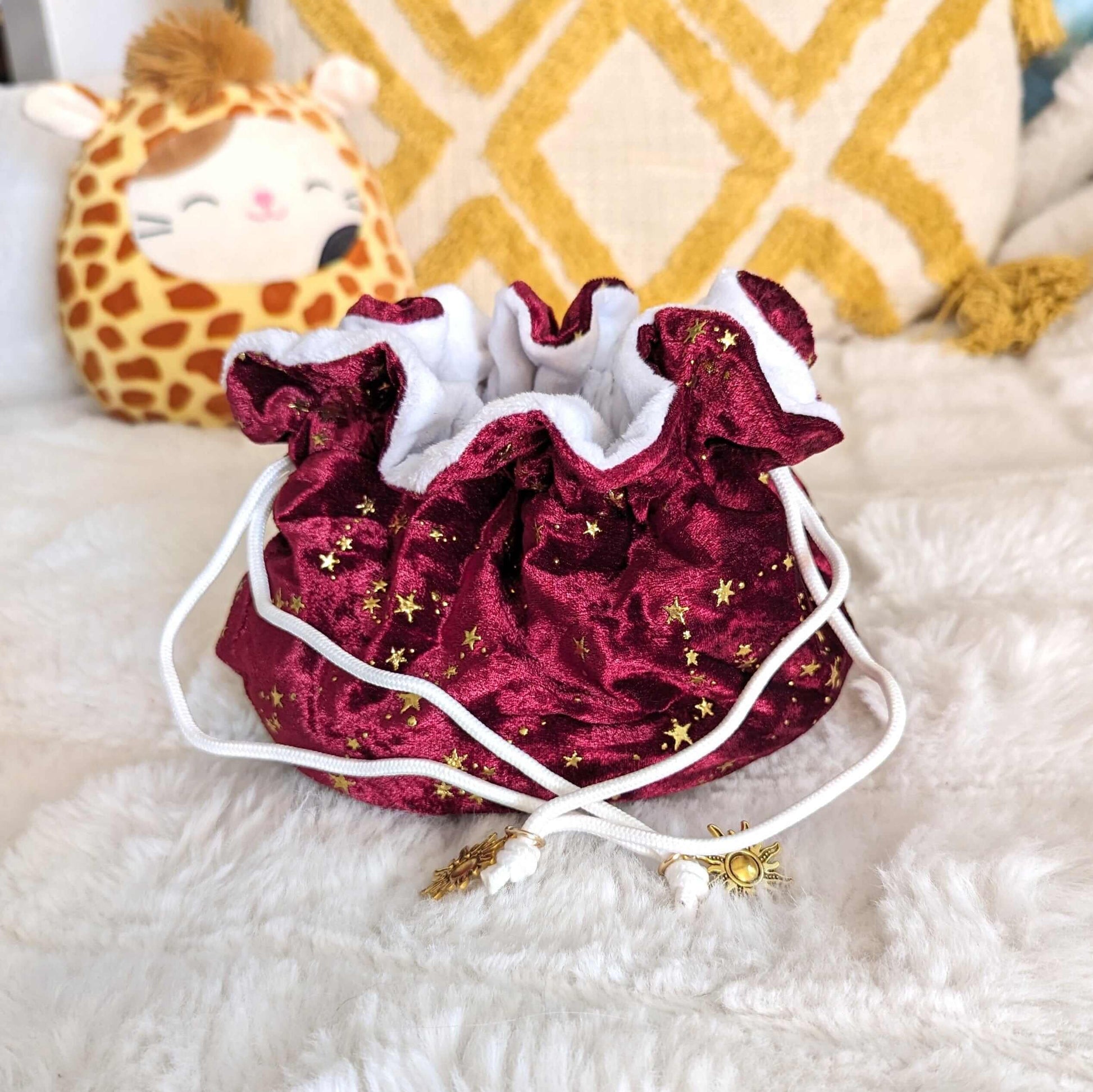 Luxurious red velvet dice bag with golden stars, white plush lining, and elegant drawstrings featuring sun charms, perfect for tabletop gamers.