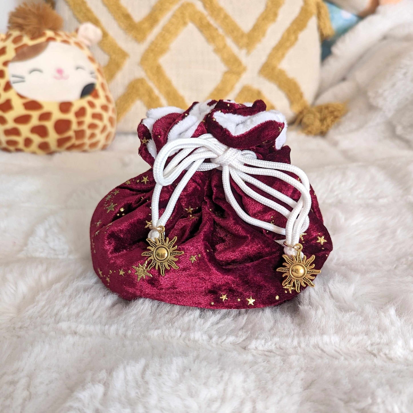 Luxurious red velvet dice bag with golden stars, multi-pocket design, strong white drawstrings with sun charms, on plush fabric background.