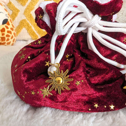 Luxurious red velvet dice bag with gold star accents and sun charm drawstring, perfect for tabletop gamers.