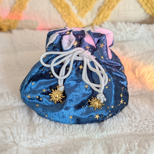 Starry teal dice bag with gold star design and solar charms on drawstrings, displayed on a cozy background.