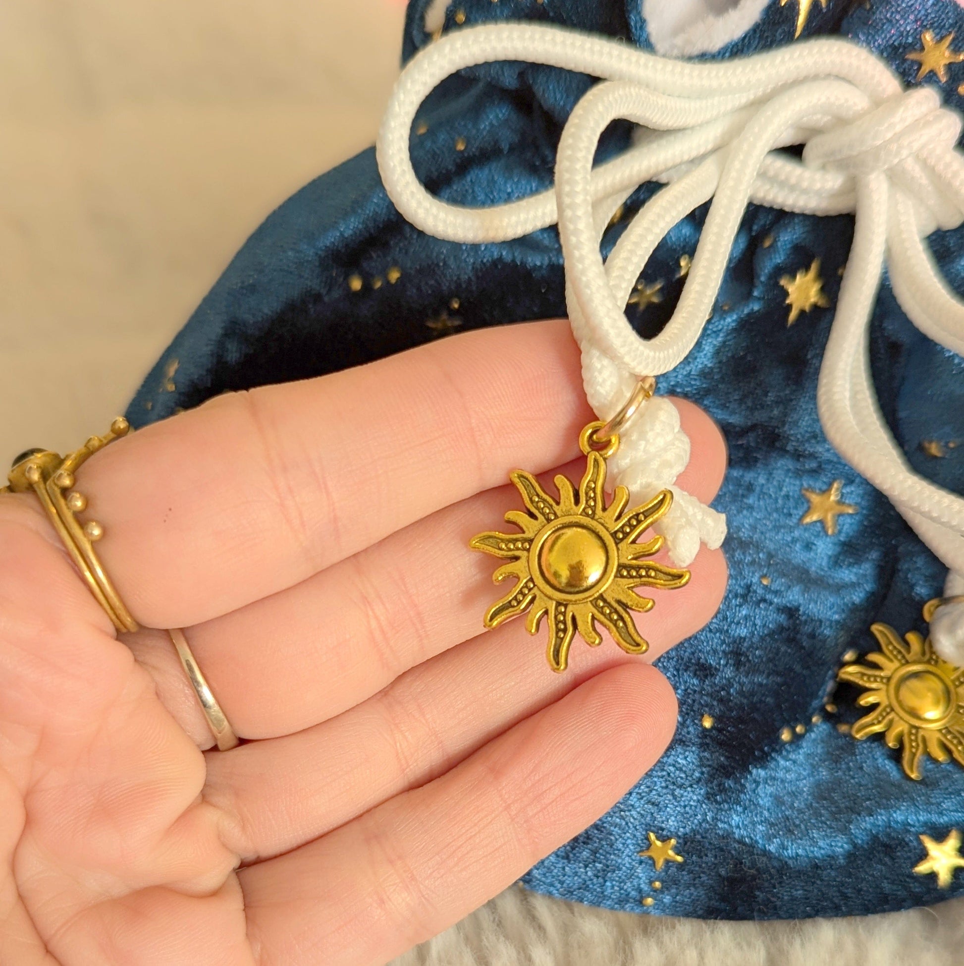 Close-up of a teal dice bag with gold star design and drawstrings featuring gold solar charms.