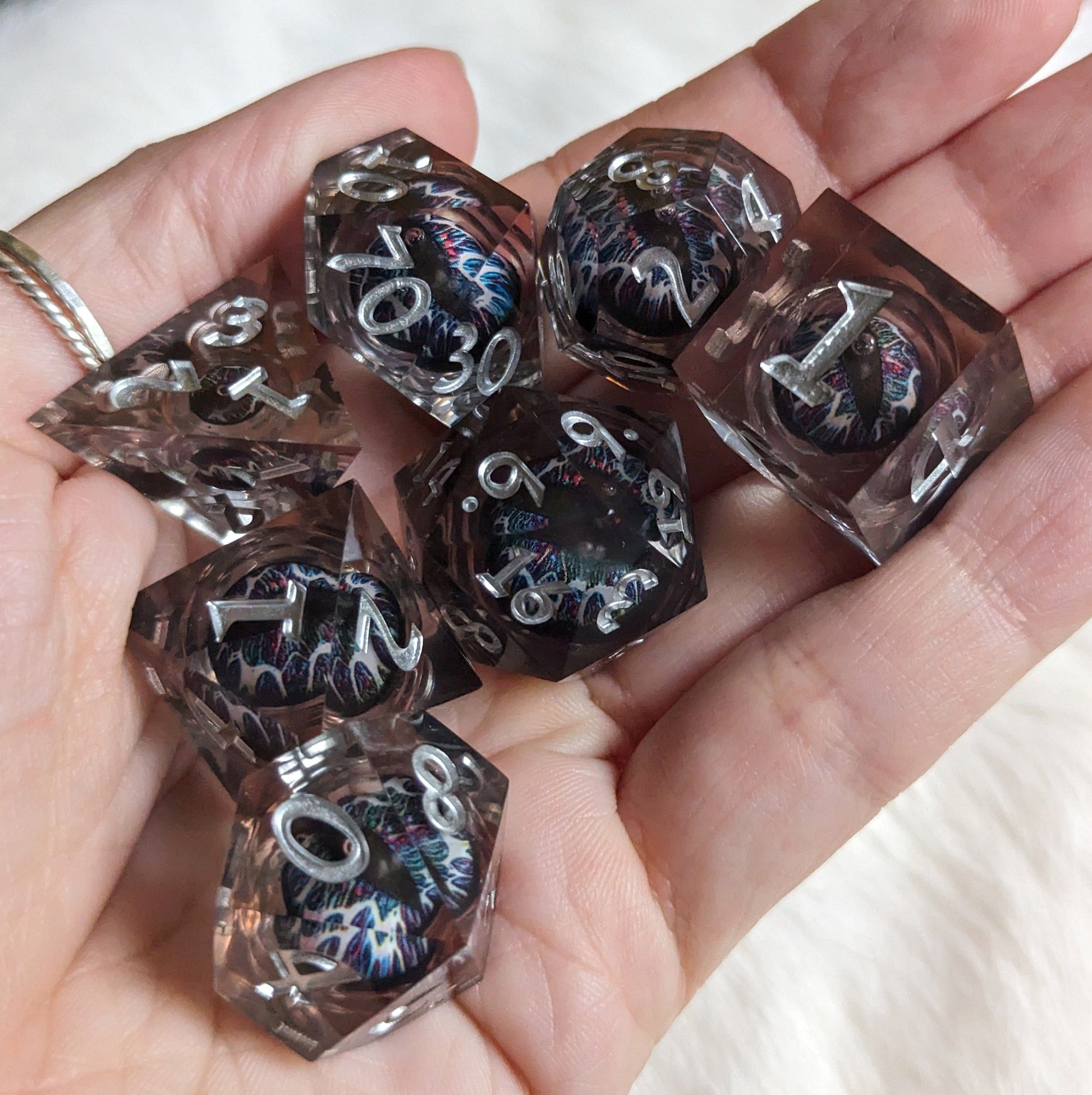 Technicolor Moving Eye Liquid Core Dice Set with swirling colors displayed on a hand for tabletop gaming.