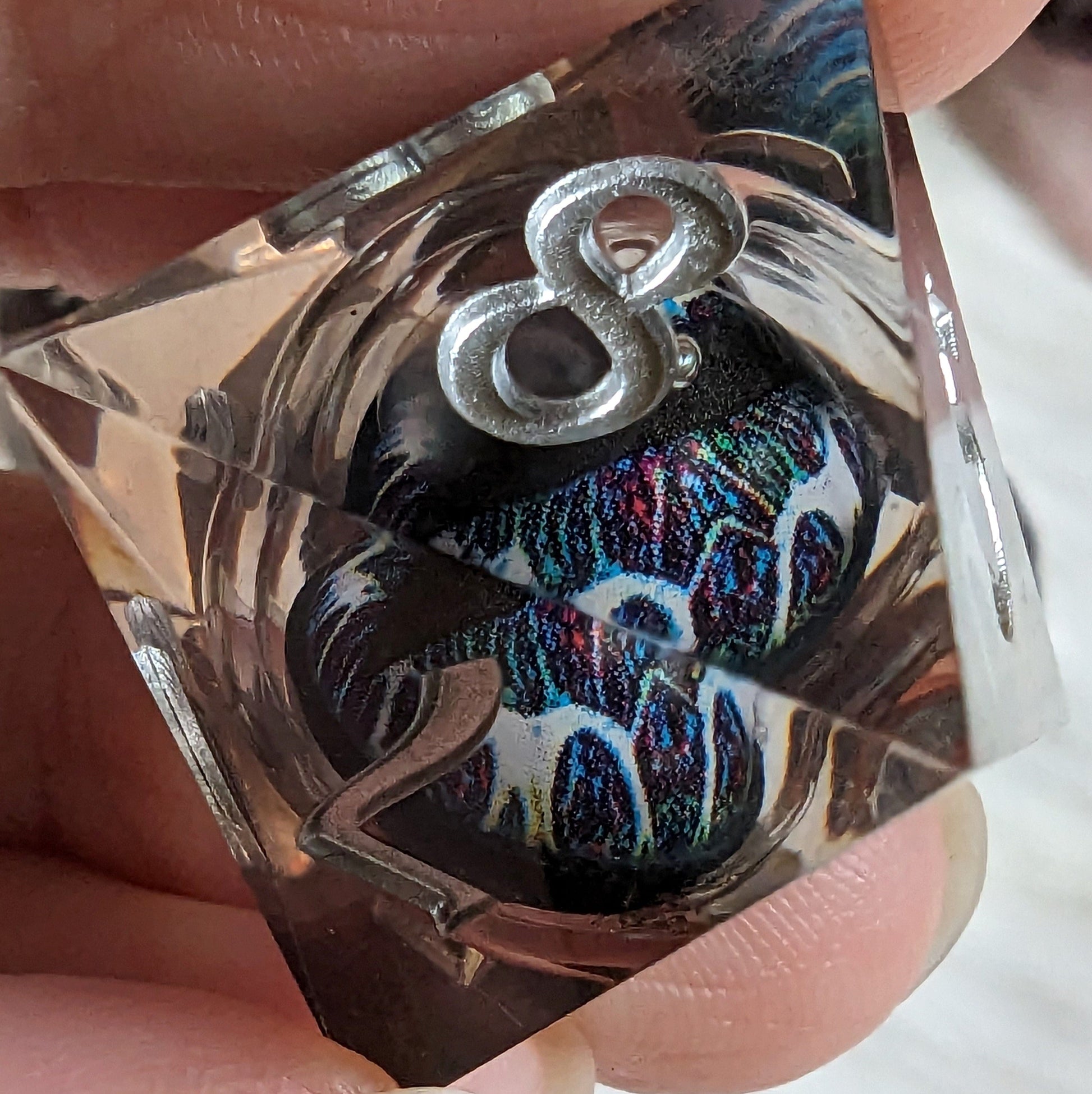 Close-up of a technicolor liquid core die with dynamic swirling colors and an eye design inside a polyhedral dice set.