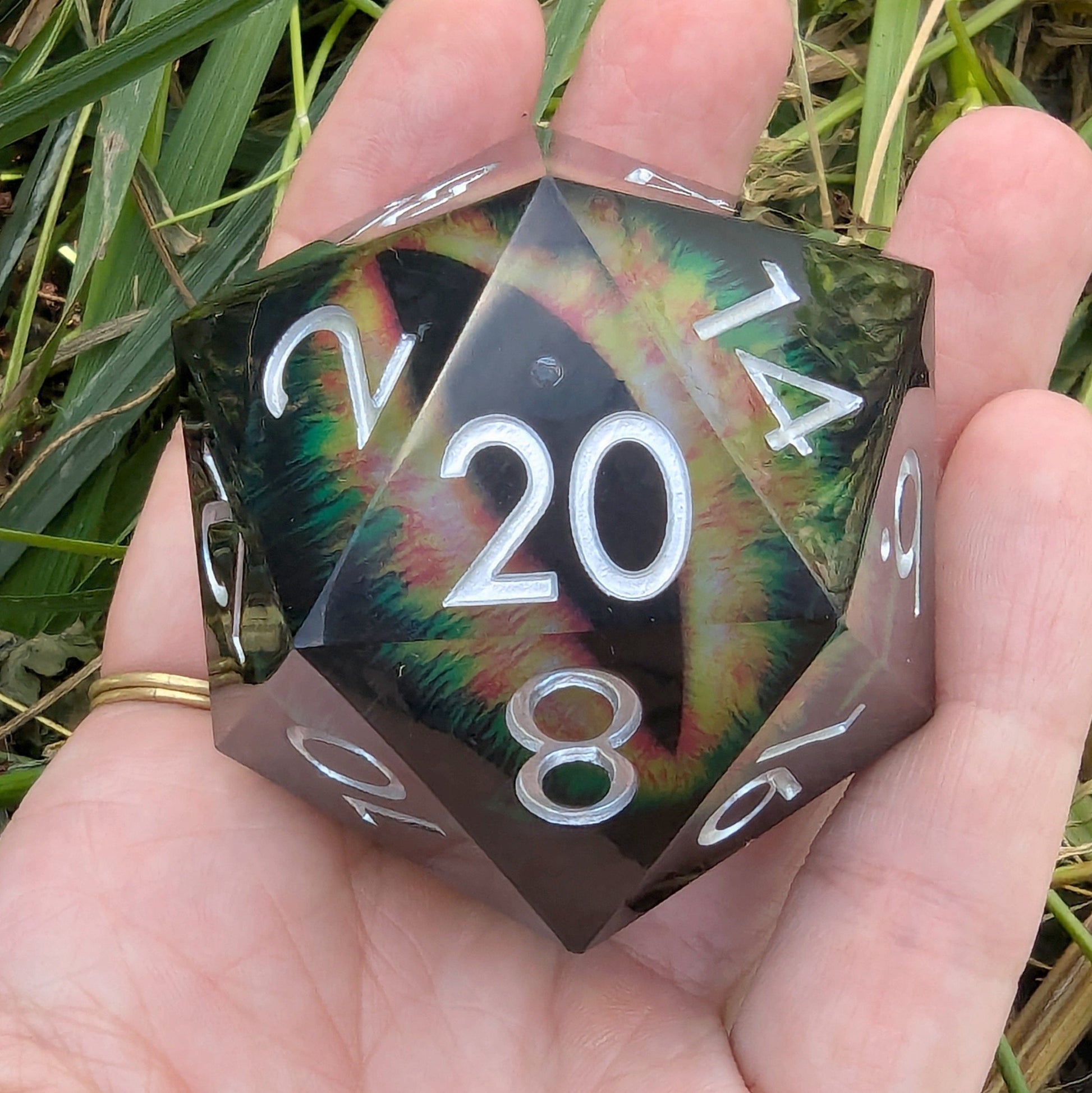 Hand holding The Infernal Watcher giant D20 die with vivid eye design and dark resin case.