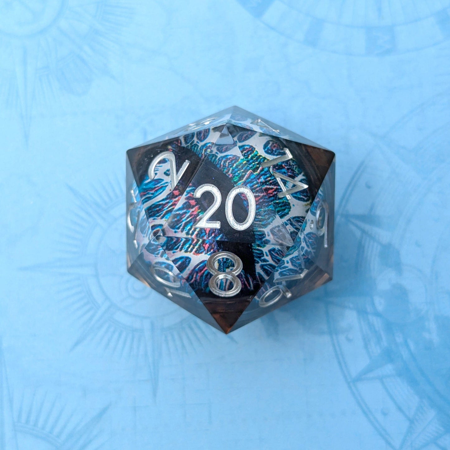 Clear resin D20 with vibrant eye design and numbers on a blue background, featuring blue, black, and pink hues inside.