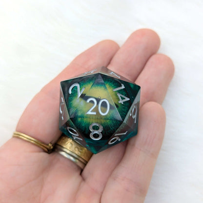 Hand holding The Watchful Eye large D20 die with green resin and liquid core featuring a vivid eye design.