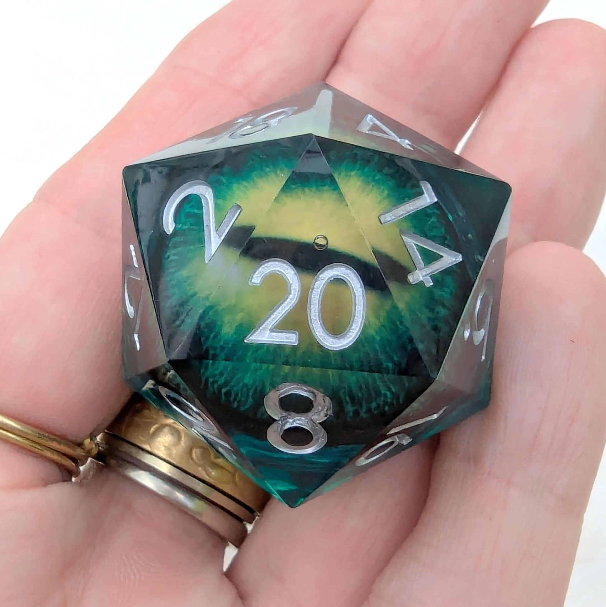 Large green D20 die with a vivid green and yellow eye inside, held in a hand.