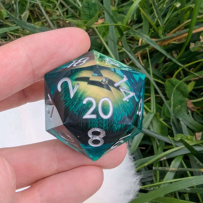 Oversized green resin D20 dice with shifting eye core, held in hand against grassy background.