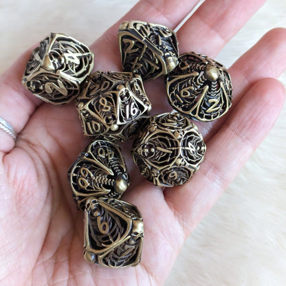 Hand holding a 7-piece Vampire Skeleton Hollow Metal Dice Set with intricate skeleton designs for tabletop role-playing games.