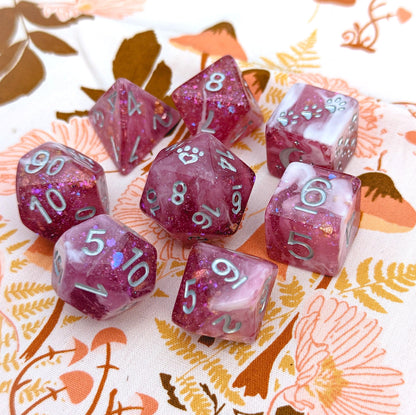 Berry Wine 8 Piece Dice Set in clear burgundy resin with glitter and foil, featuring custom cat wizard and paw designs by Fennek & Finch.