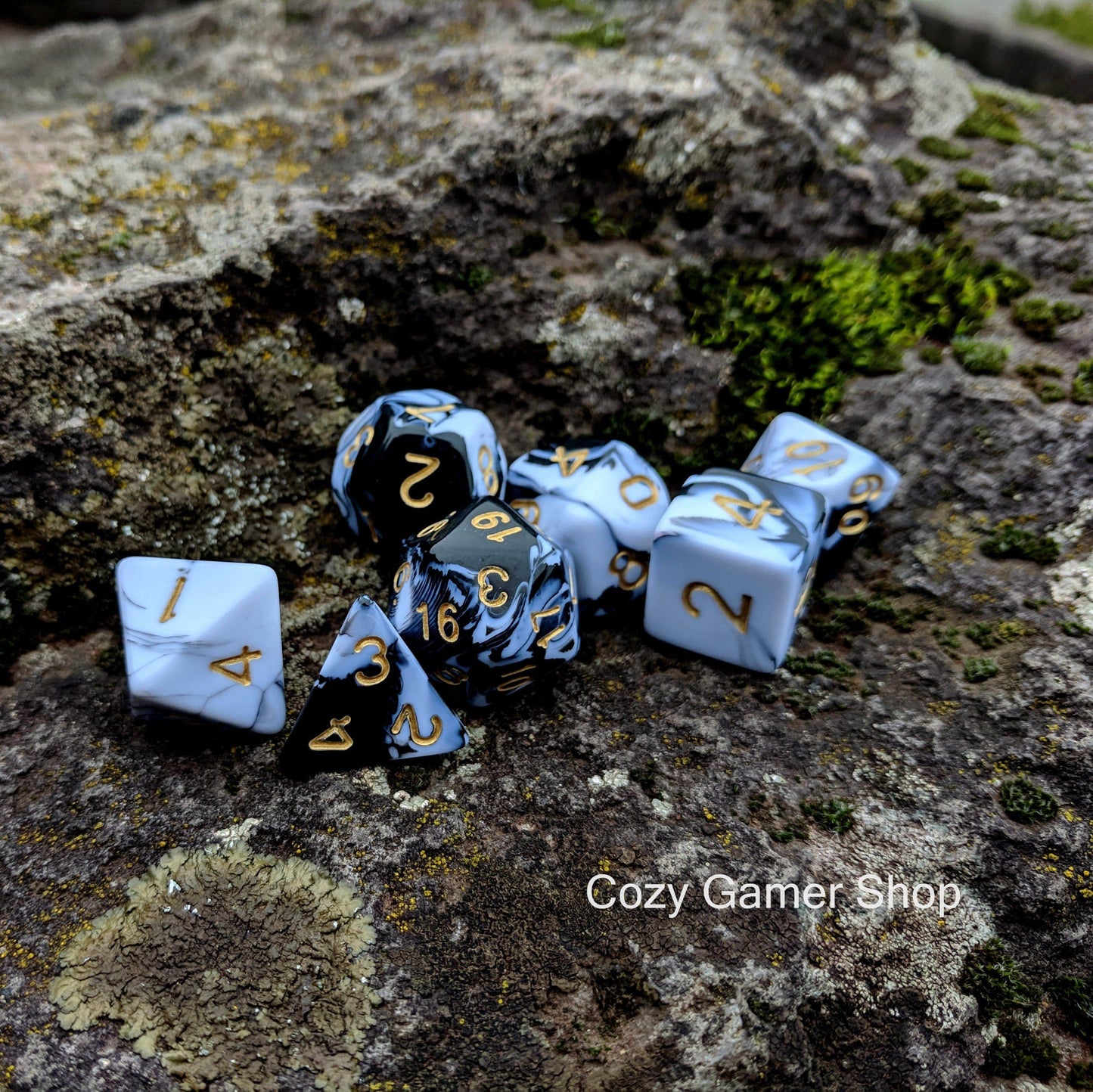 Black and white marble dice set on mossy rocks, 7-piece polyhedral acrylic set for tabletop games.