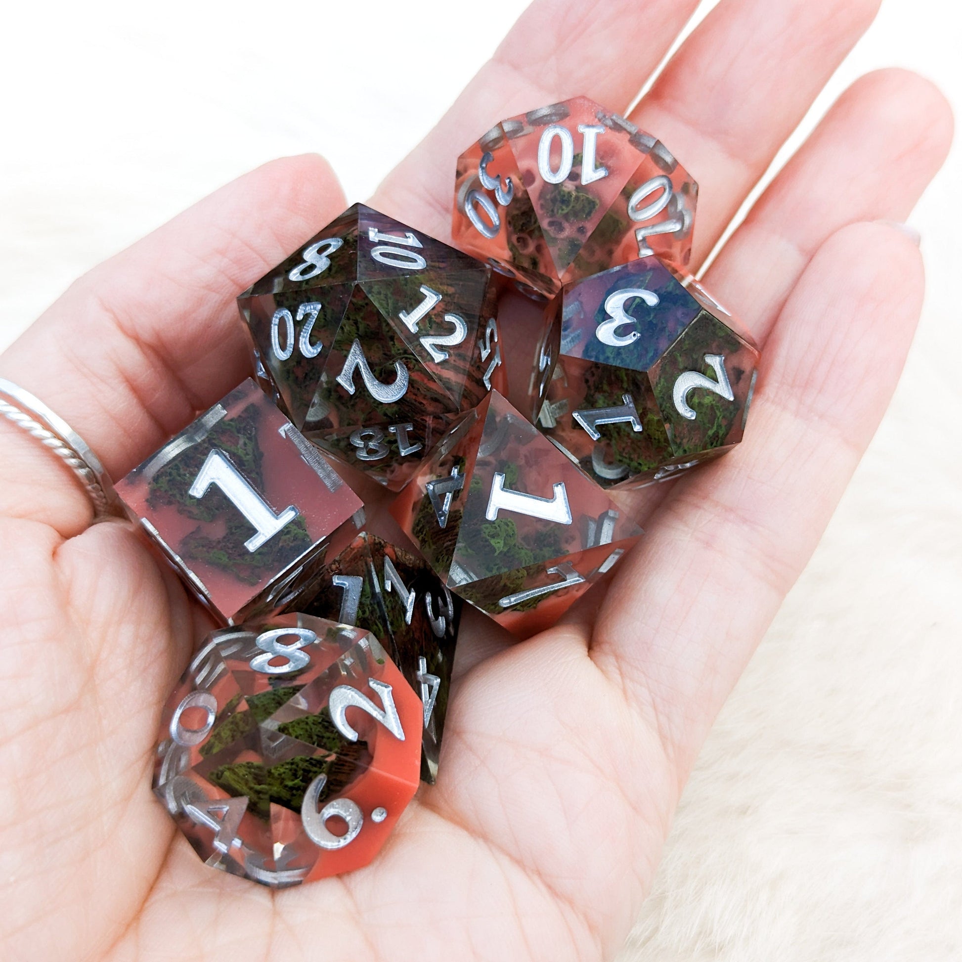 Blood Mountain Sharp Edge Resin DnD Dice Set with stone forested mountains and red misty clouds in a hand.