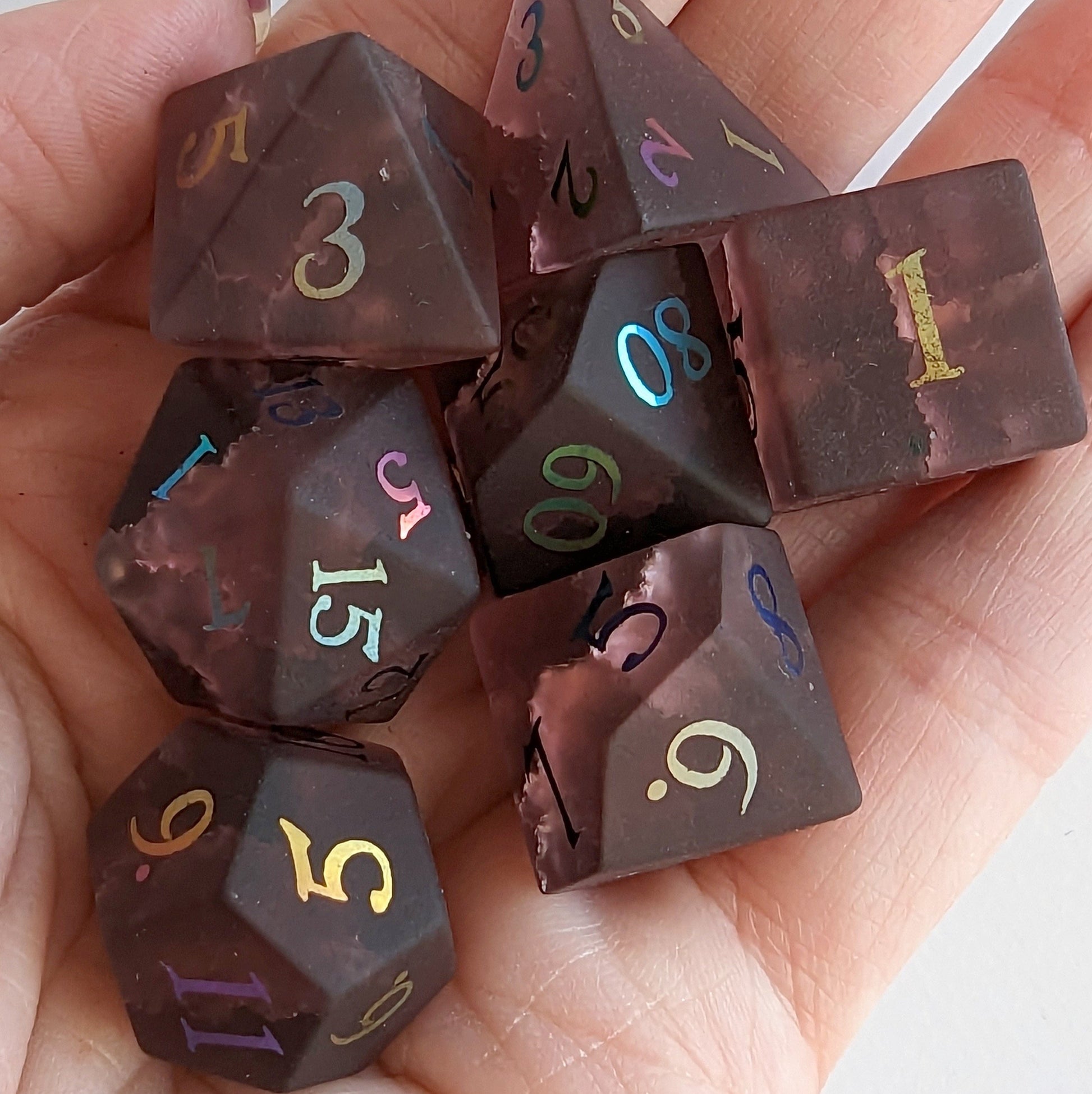 Burgundy crackled glass dice set with colorful numbers held in hand, includes standard 7-piece set for DnD gaming.