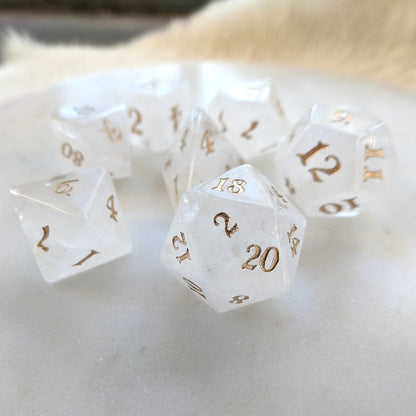 Clear Quartz Dice Set with gold numbers, real gemstone 7 piece TTRPG dice on marble surface, ideal for fantasy tabletop games.