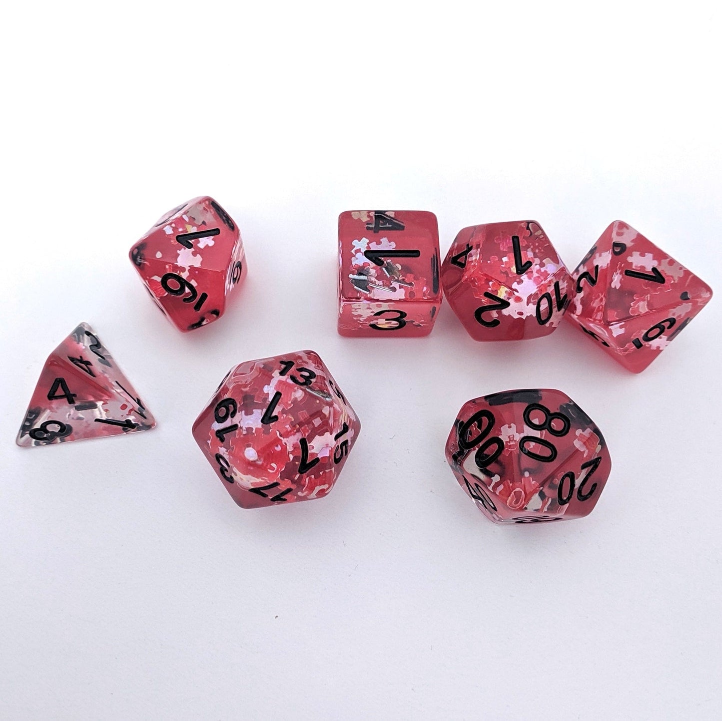 Red translucent glitter DnD dice set with black numbers and puzzle piece glitters, perfect for tabletop role-playing games.