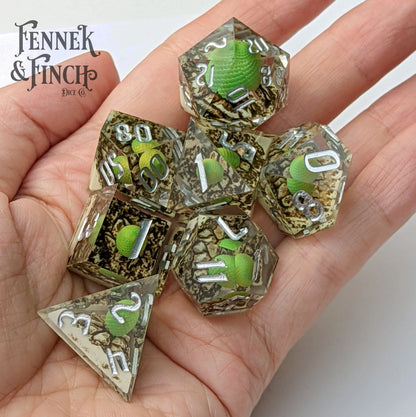 Dragon Egg Sharp Edge Resin Dice Set with green dragon eggs and silver numbers, 7 piece TTRPG dice set in hand.