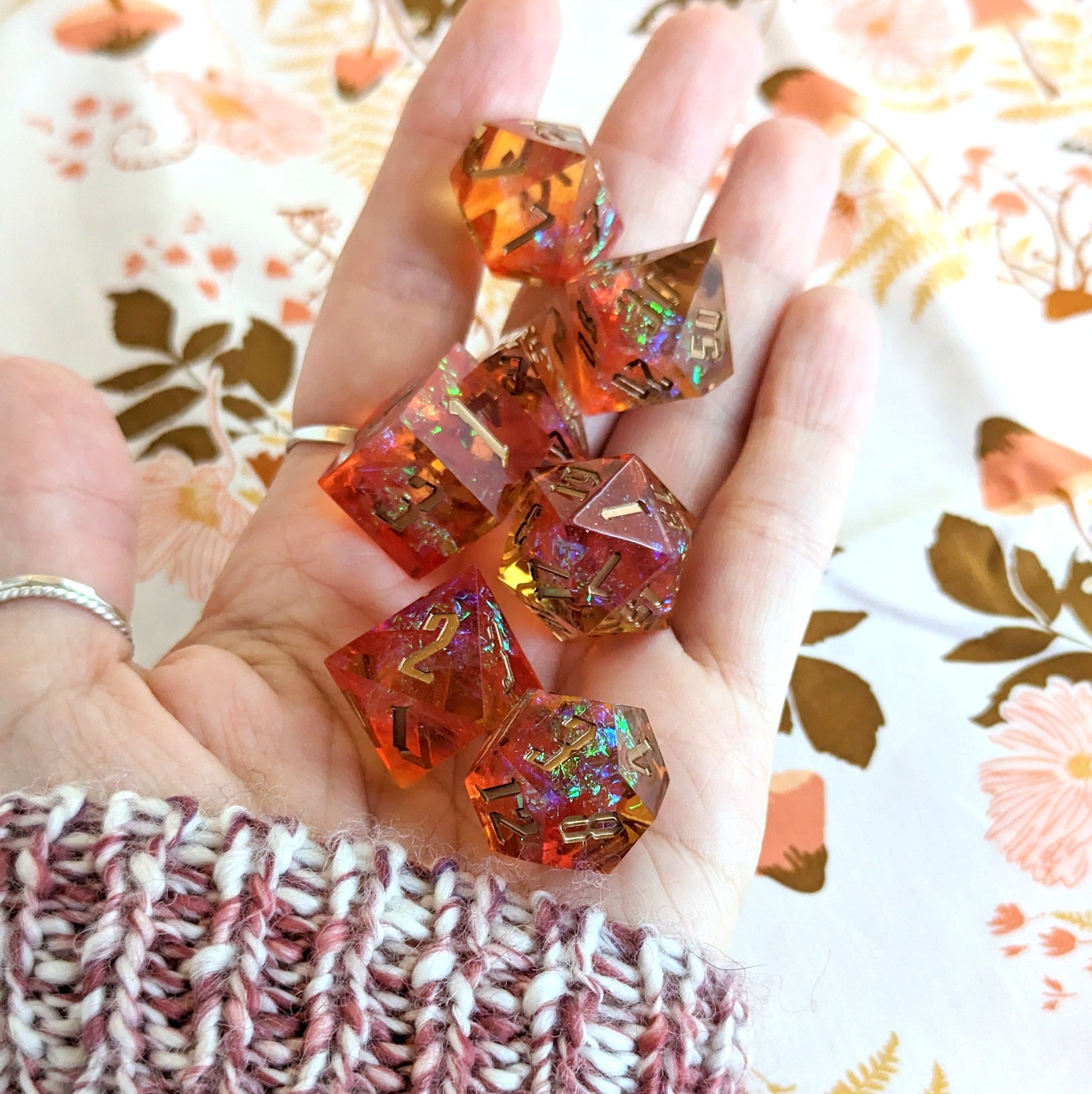 Hand holding fiery red and gold iridescent sharp edge resin dice set for TTRPG, perfect for DND adventures.