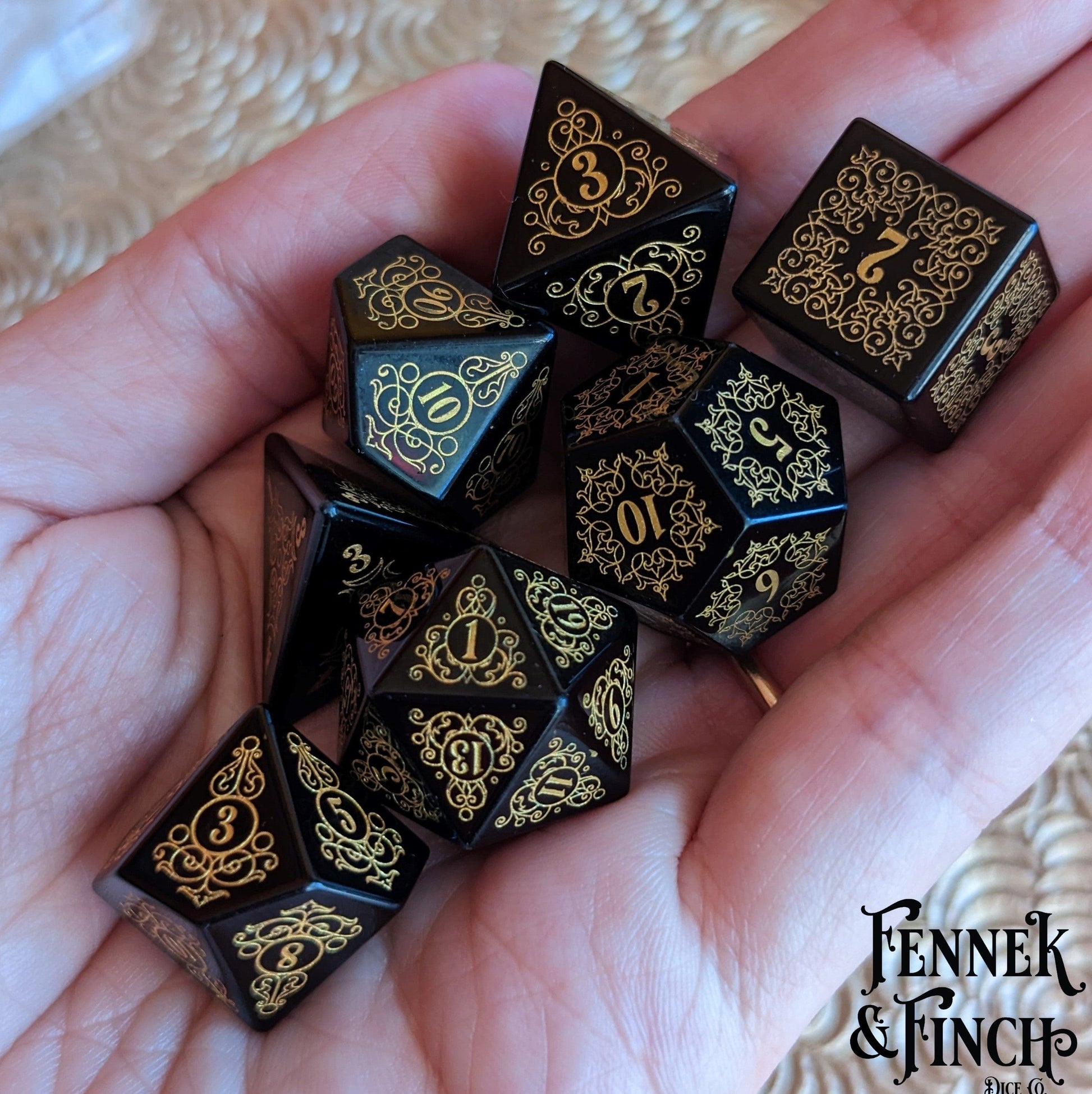 Hand holding Garden Gate Obsidian Gemstone Dice Set with intricate gold floral patterns, showcasing enchanting volcanic design.