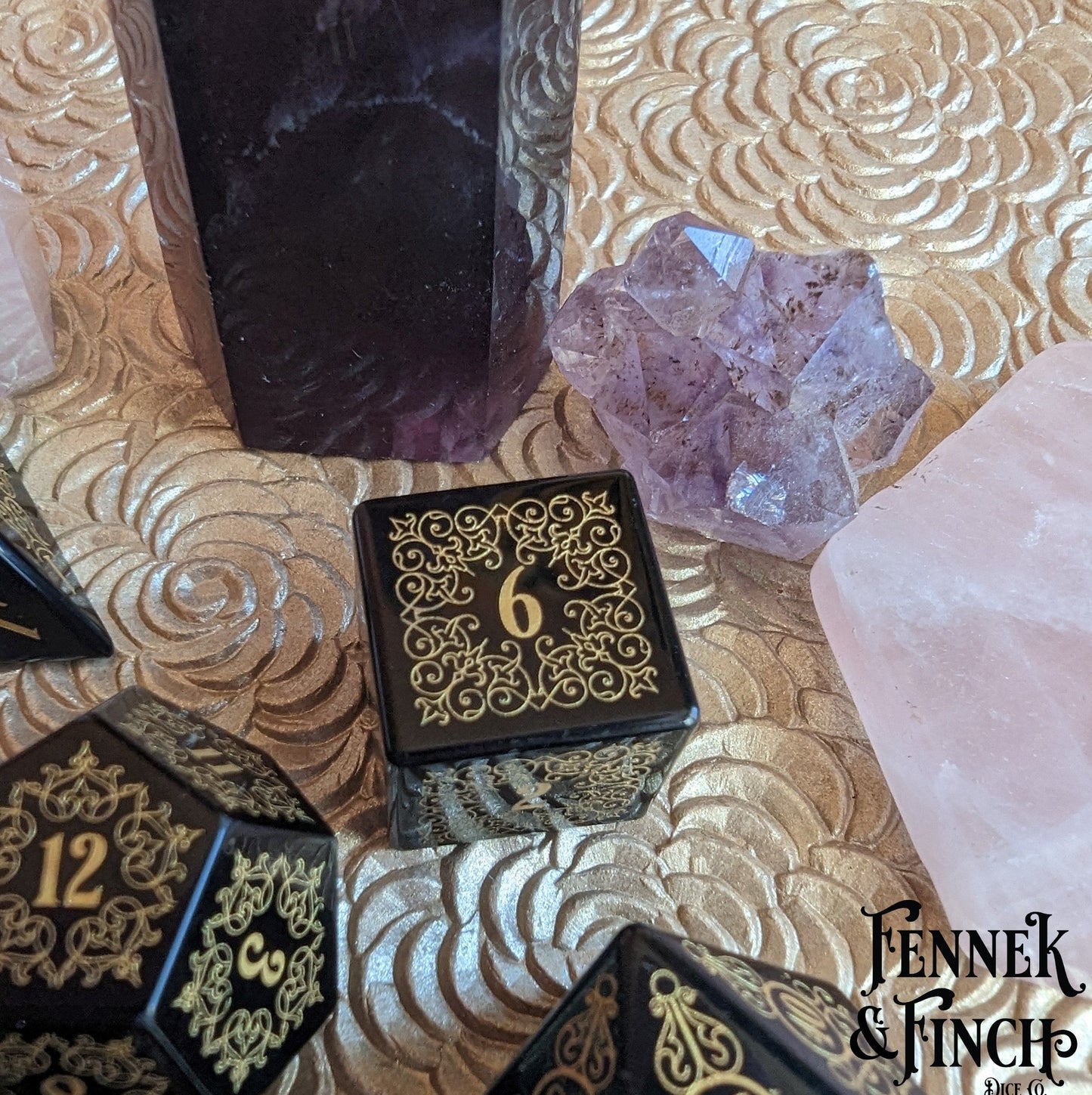 Garden Gate Obsidian Gemstone Dice Set with intricate floral patterns surrounded by amethyst and rose quartz crystals.