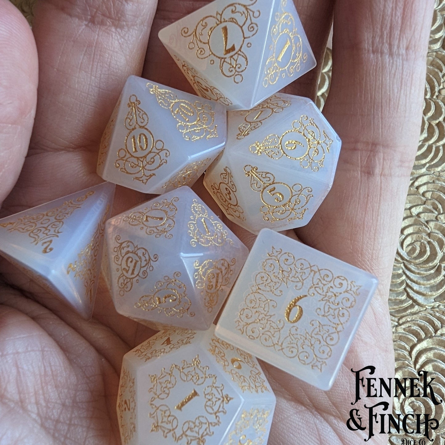 Garden Gate opalite gemstone dice set with intricate gold designs, inspired by nature's patterns, displayed elegantly in a hand.