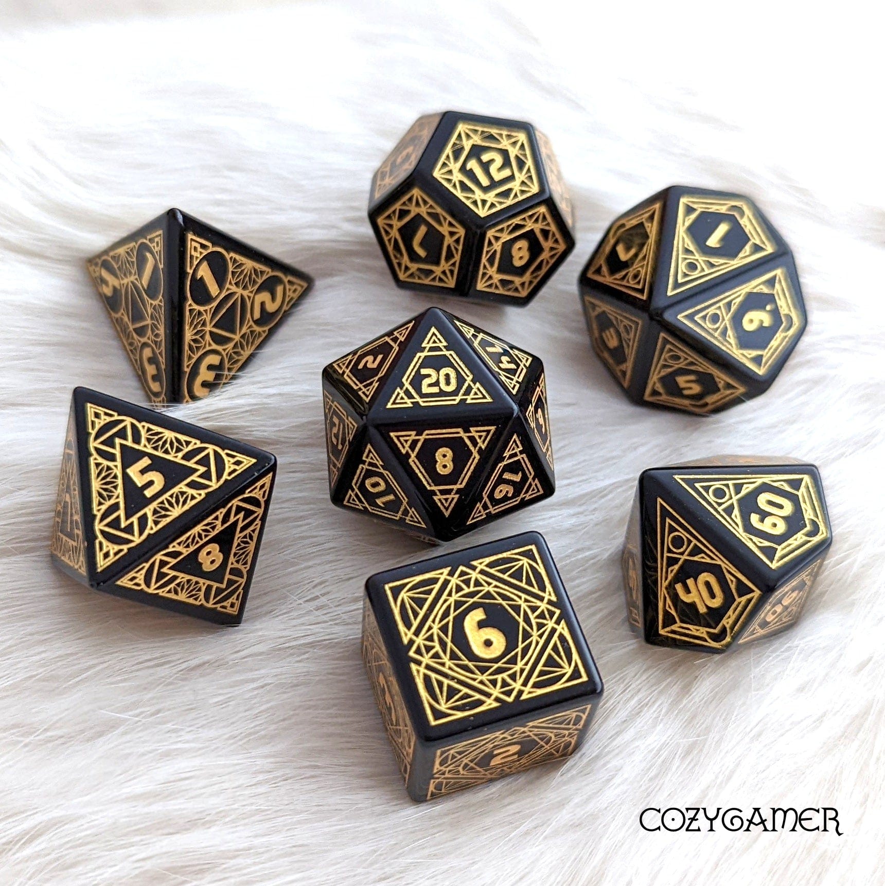 Geometric obsidian gemstone dice set with intricate gold etching on a white surface, featuring a range of polyhedral shapes.