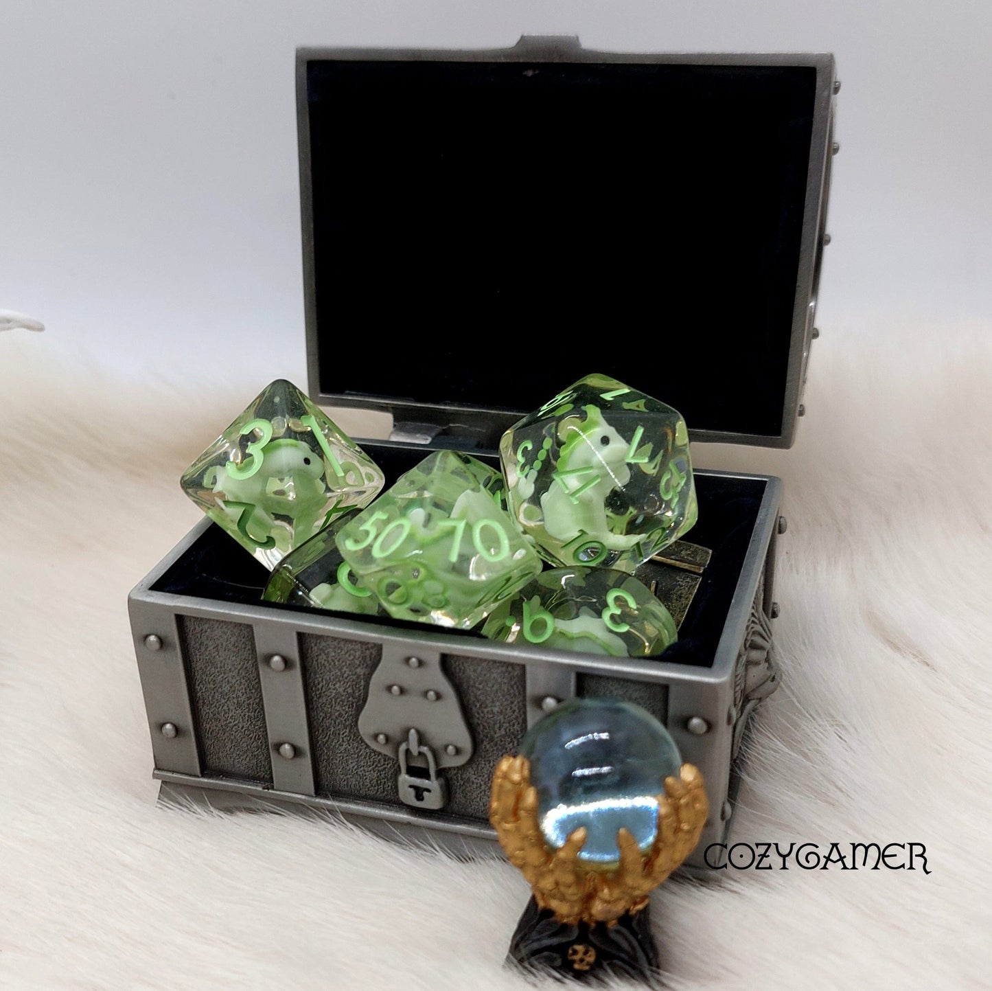 A set of green translucent dice with tiny dinosaurs inside displayed in an open treasure chest for tabletop role-playing games.