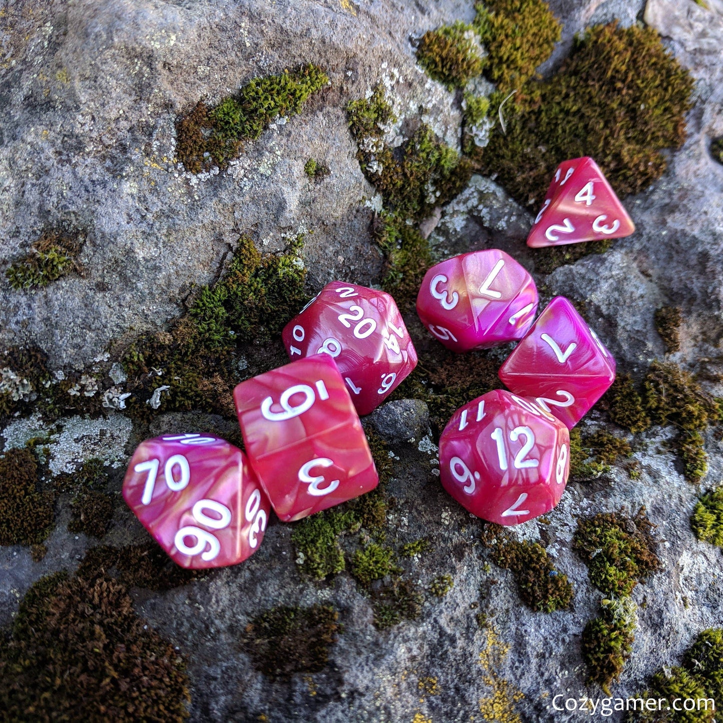 Magenta Rose marbled polyhedral dice set for Dungeons and Dragons on mossy rock background.