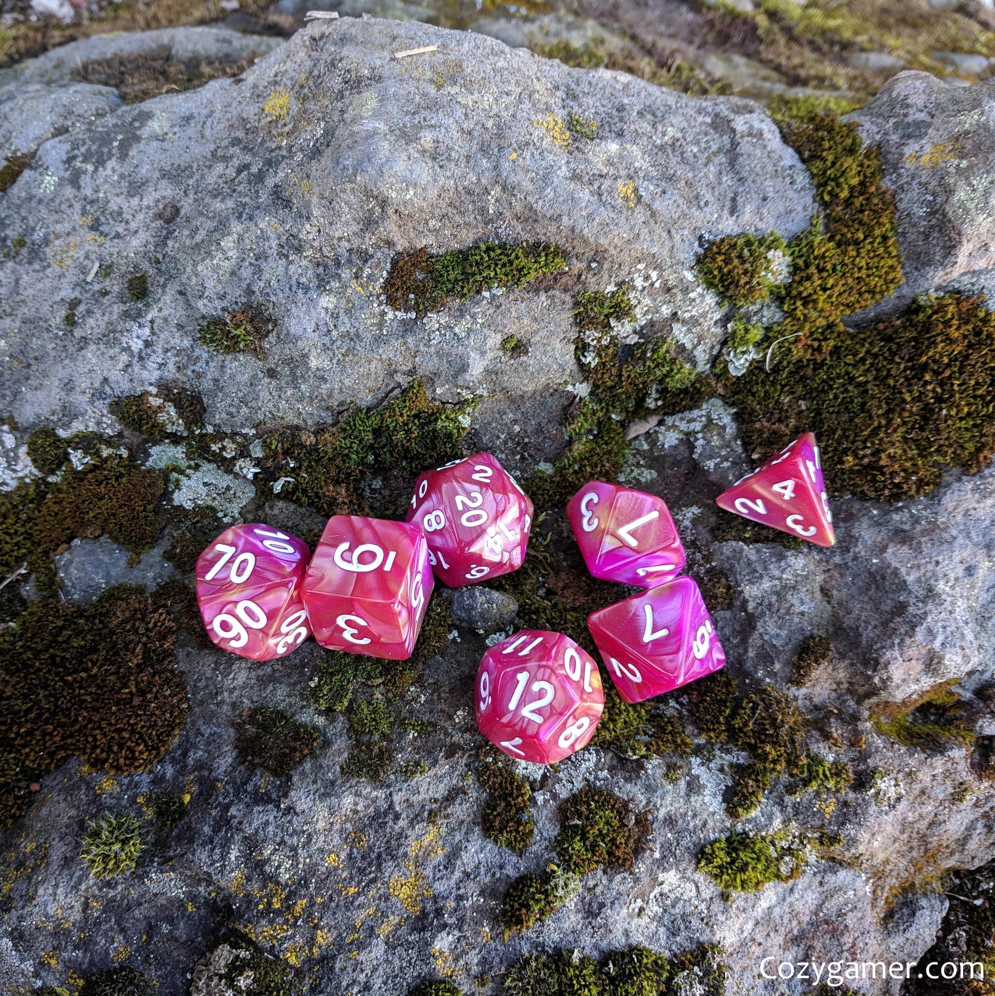 Magenta Rose DnD Dice Set with marbled pearly dark pink and orange design on a moss-covered rock background.