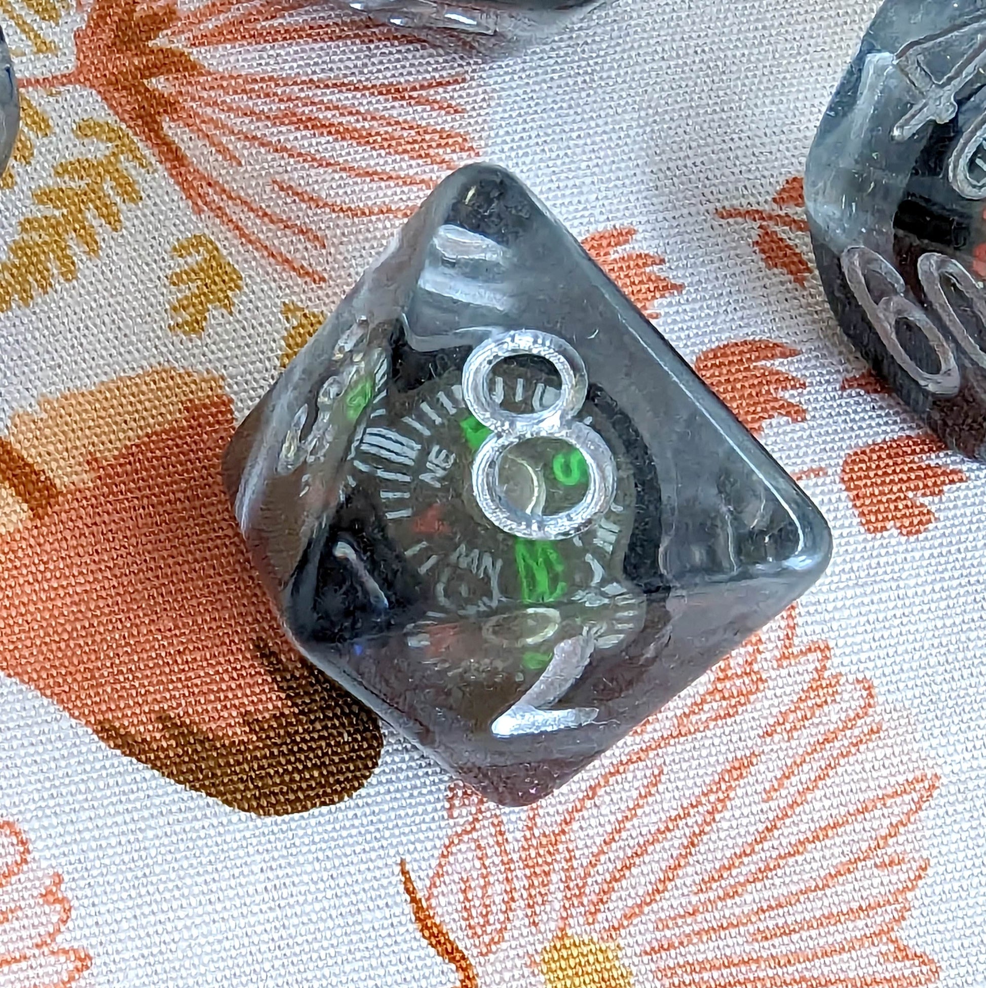 Crystal clear dice with embedded mini compass from 7 piece TTRPG set for Dungeons and Dragons, resting on a floral fabric backdrop.