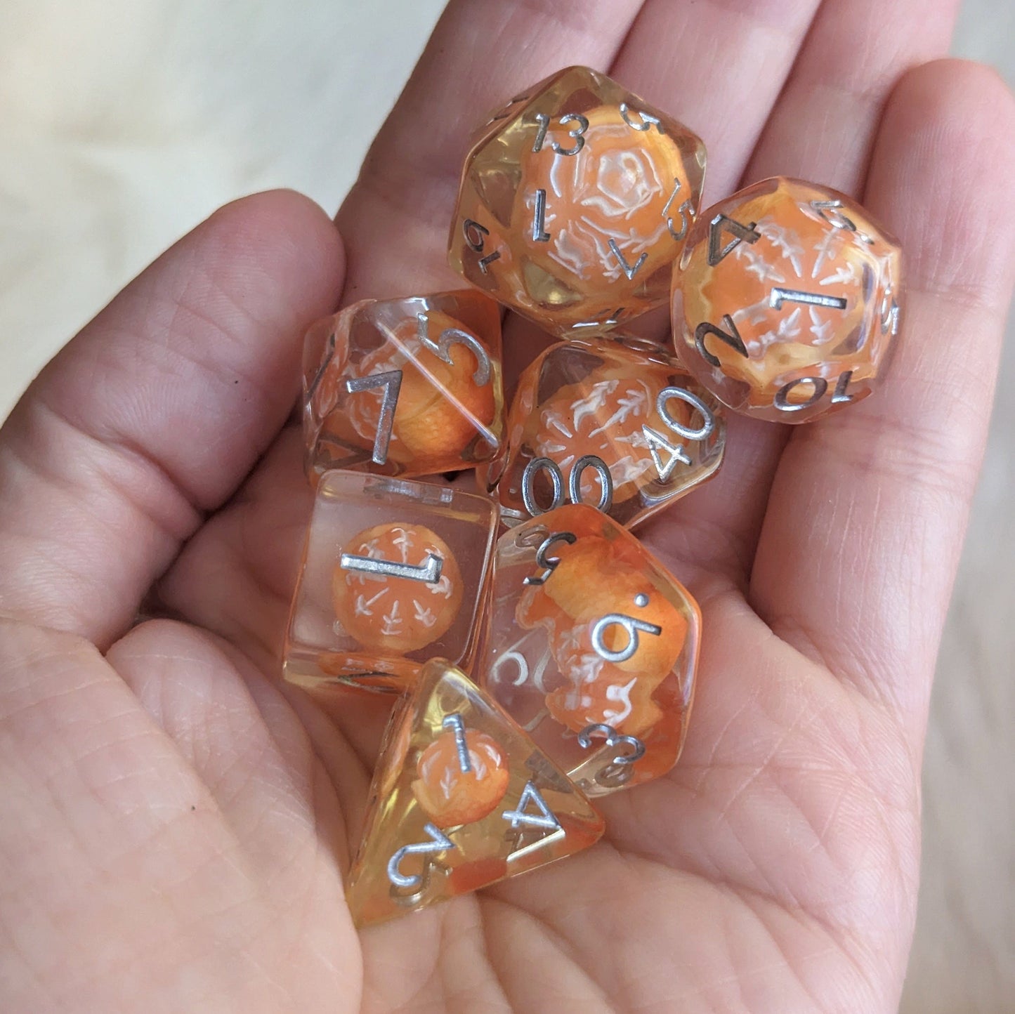 Hand holding seven-piece Peeled Orange resin inclusion DnD dice set.