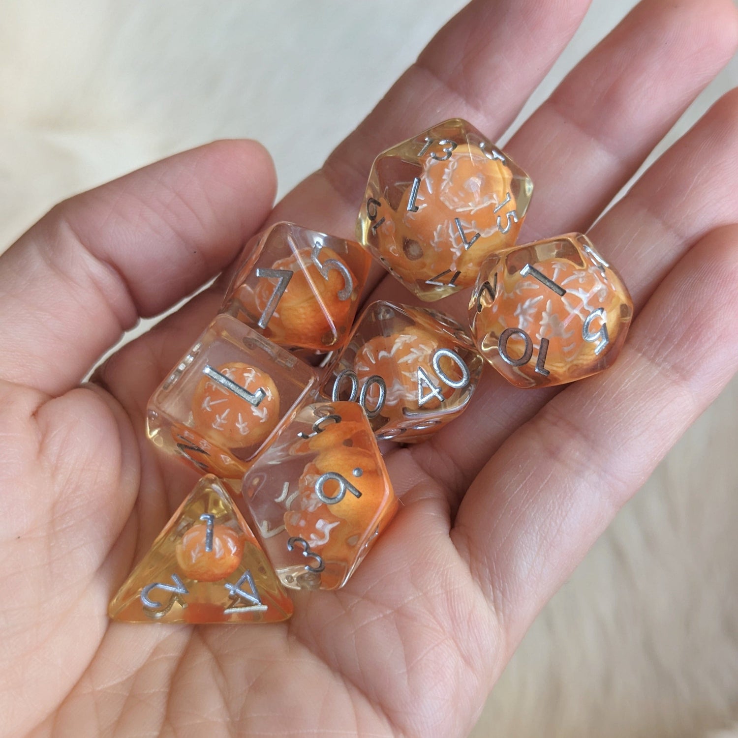 Hand holding a Peeled Orange DND dice set with resin inclusion, featuring a standard 7 piece collection against a beige background.