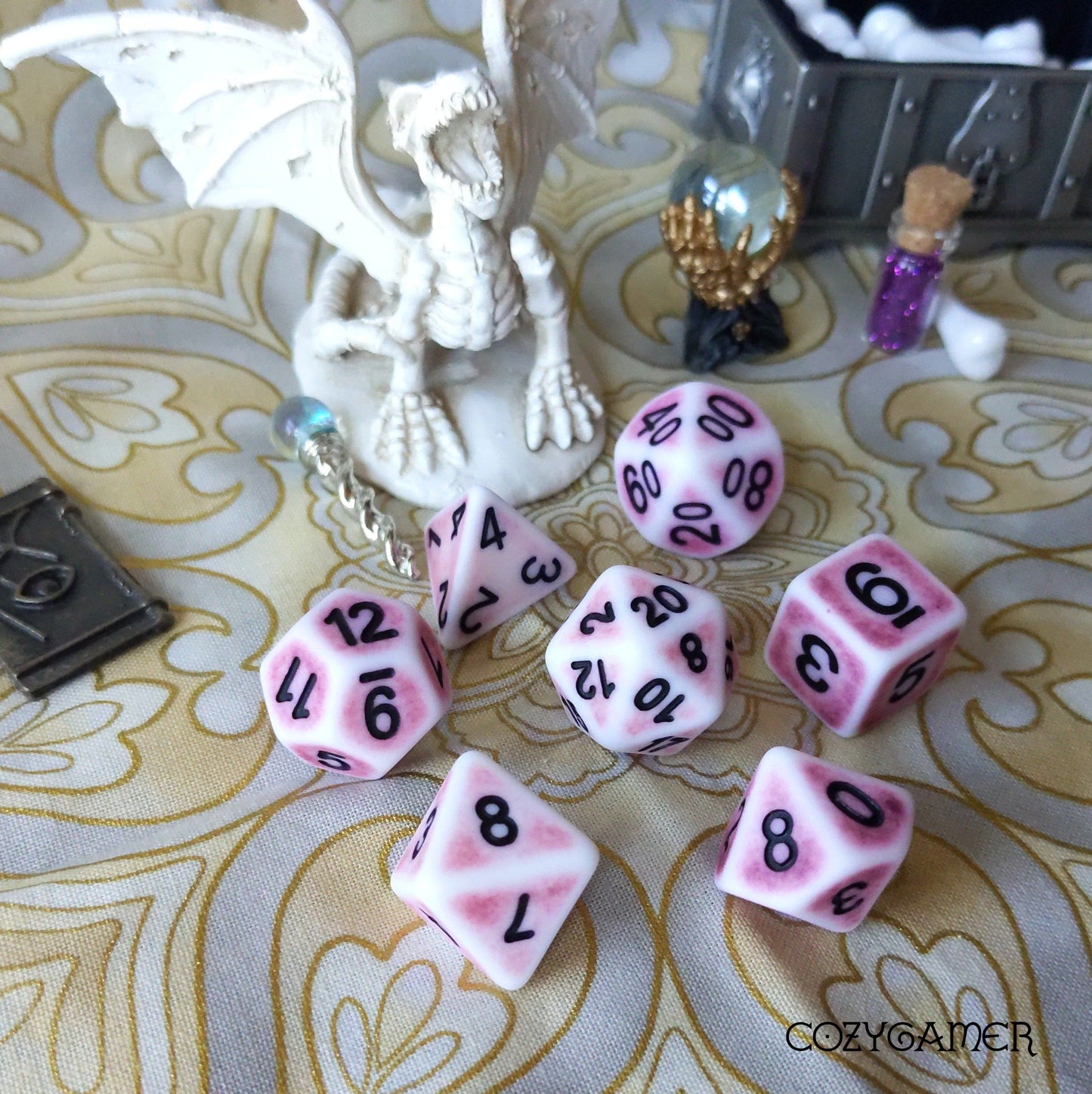 Pink Ancient Dice Set with black numbers for tabletop RPGs displayed on patterned surface.