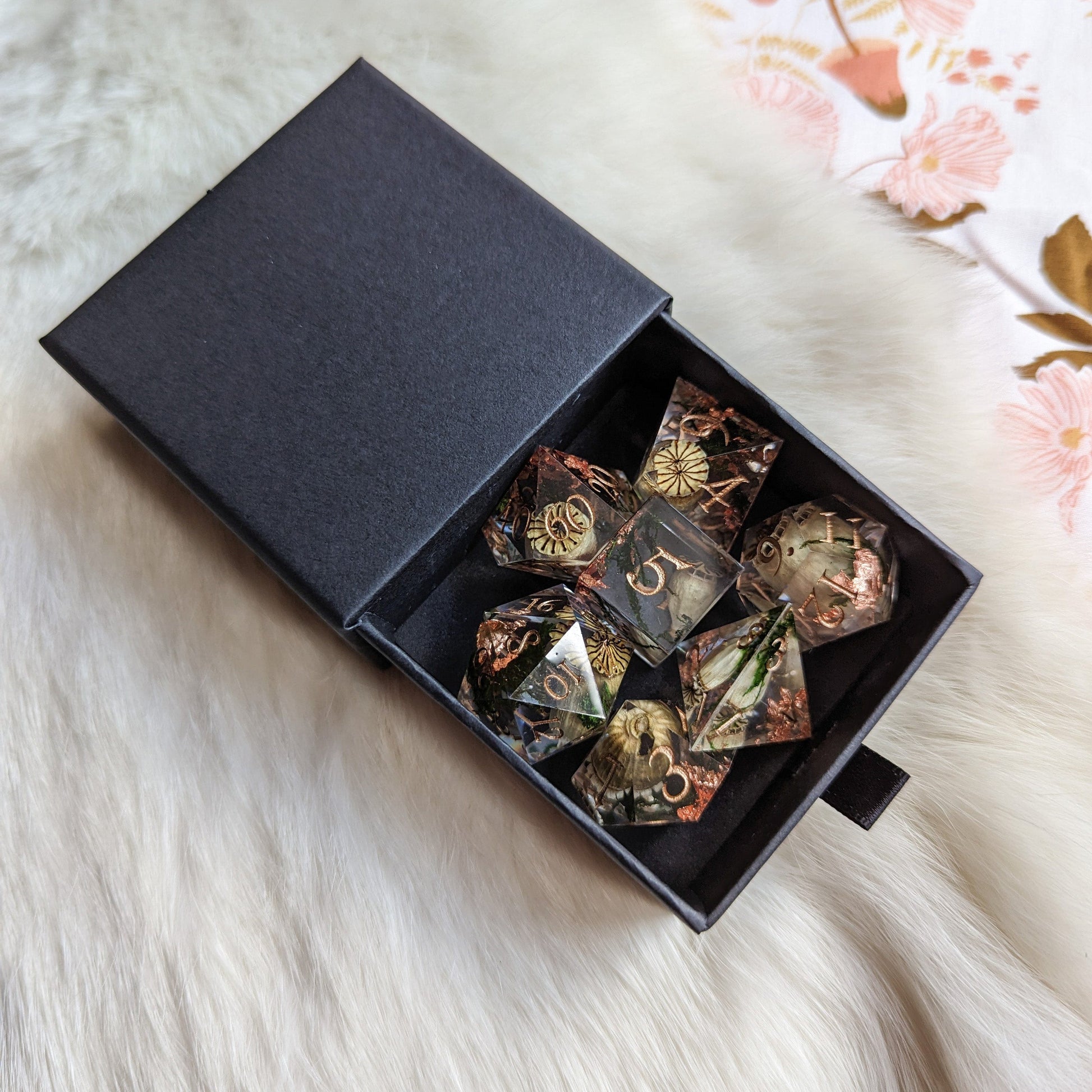 Poppy Pods and Moss 7 Piece Dice Set with dried poppy pods, moss, and copper foil in a black box on a soft surface.