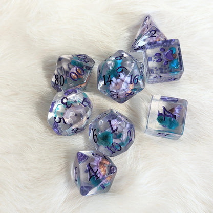 Purple and blue flower DND dice set with purple fantasy font and extra D6 with paw prints on a soft white background.