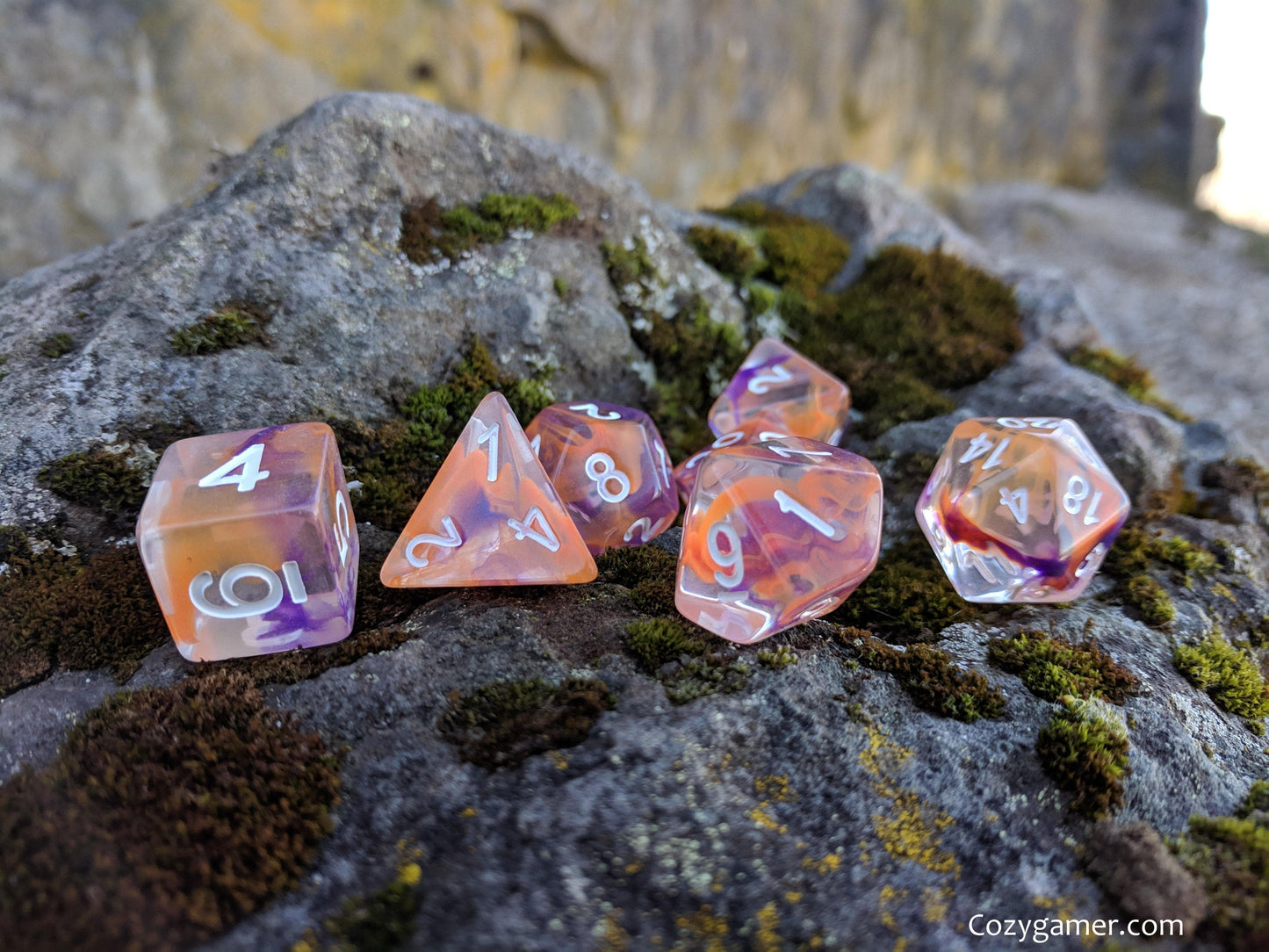 Translucent purple and orange polyhedral dice set on rocks for tabletop RPGs like Dungeons and Dragons.