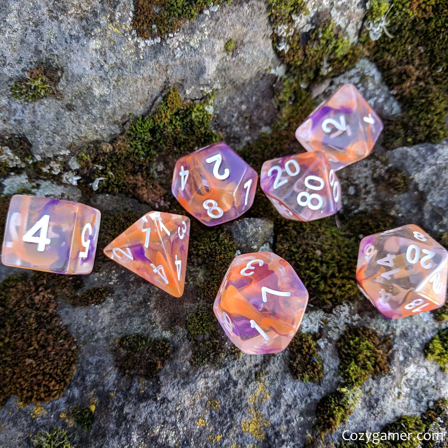 Purple and orange translucent polyhedral dice set for tabletop RPGs, displayed on a mossy rock surface.