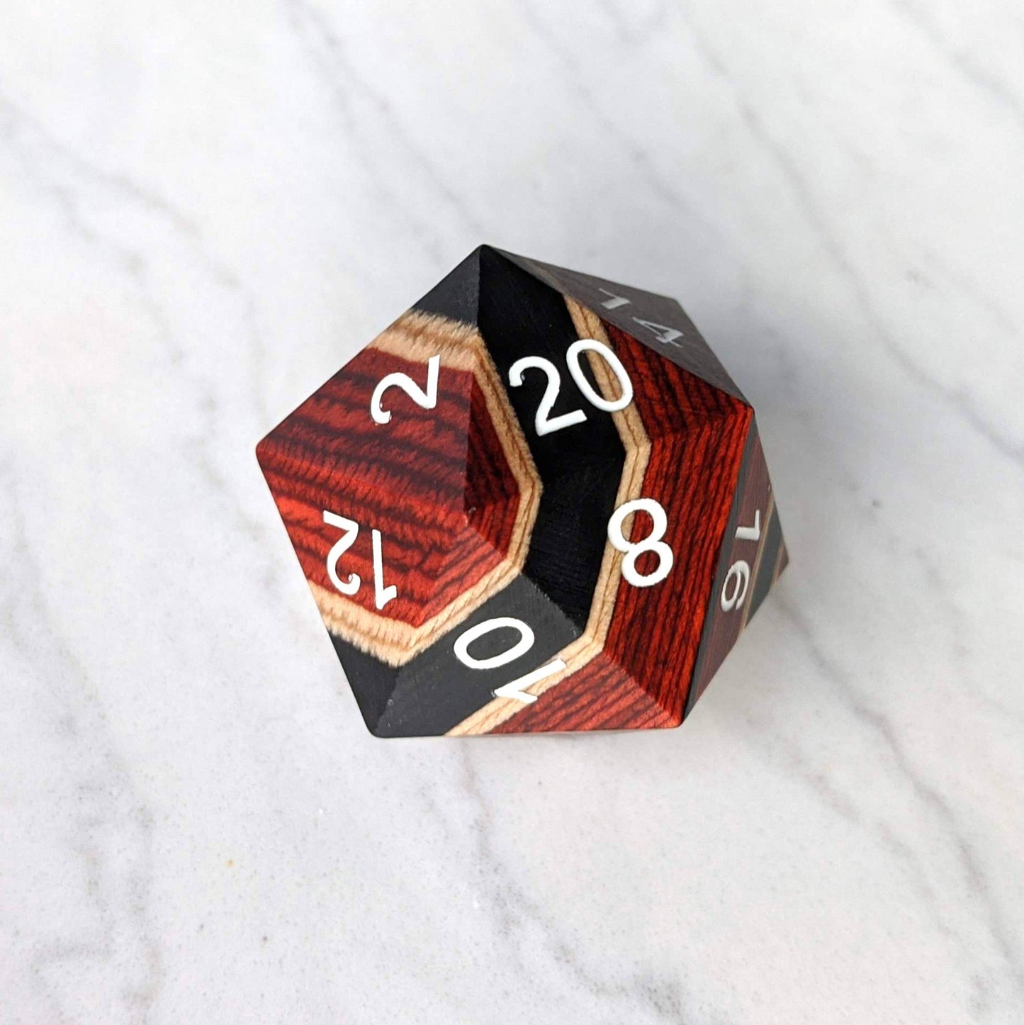 Large wooden D20 dice with red, black, and light wood stripes, featuring numbers 20, 16, 12, 8 on a marble surface.