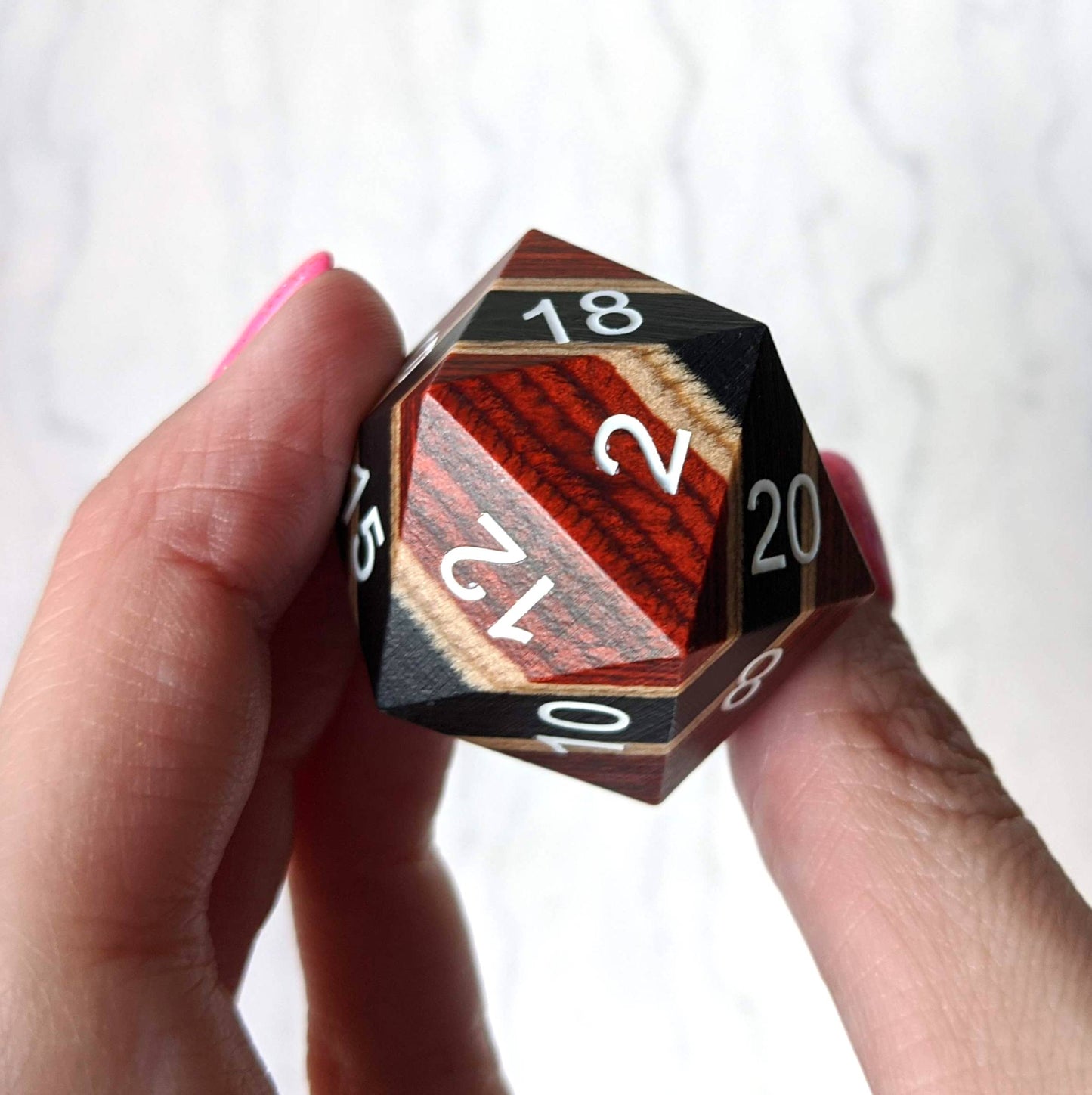 Person holding a large red, black, and light wood stripe D20 dice with numbers, ideal for gifts or collections.