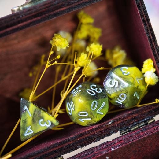 Yellow and grey acrylic polyhedral dice set for tabletop RPGs in a wooden box with yellow flowers.