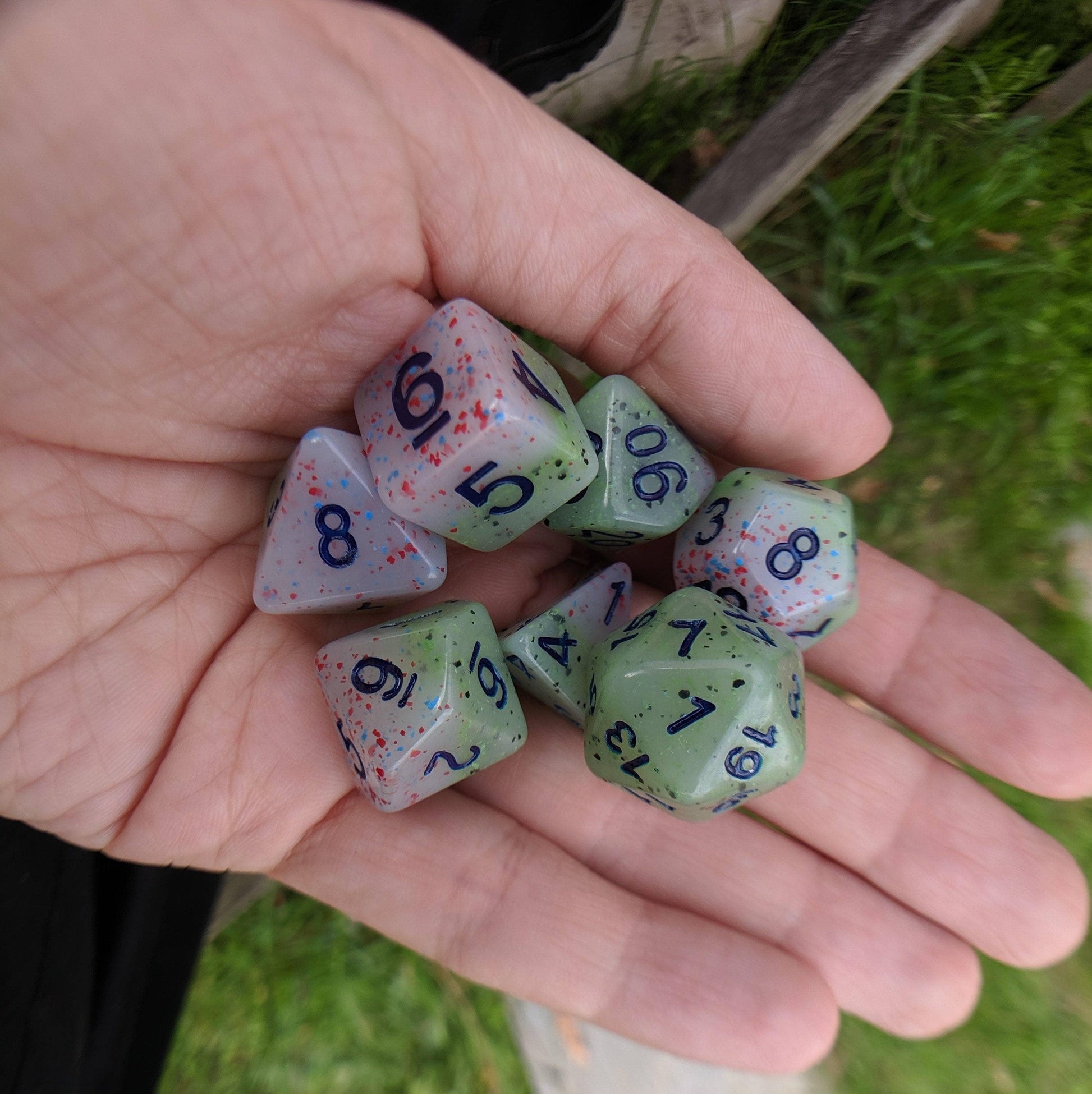 Hand holding Witch's Robe pastel layered dice set in purple and green with speckles and deep blue numbers.